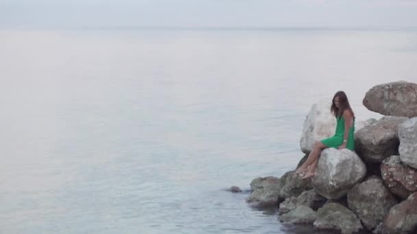 Kobieta siedzi na skały w pobliżu morza. - Materiał filmowy, wideo
