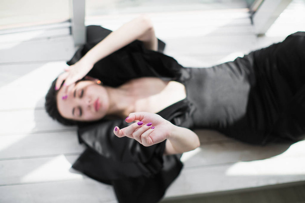 The young bewitching brunette woman in a black dress lying on the floor indoors - Fotó, kép