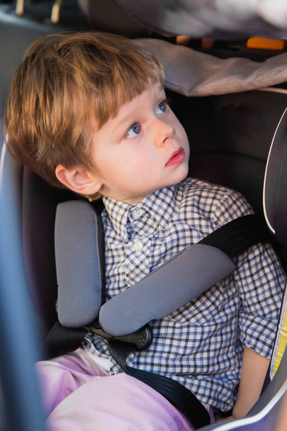 The cute little boy sitting in the baby car seat in a car and looking aside - Foto, afbeelding