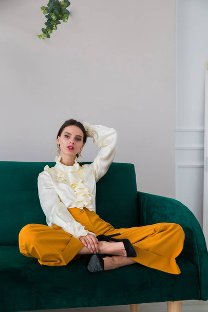 The gorgeous, serious, stylish young woman sitting on a green sofa indoors - Foto, Imagen
