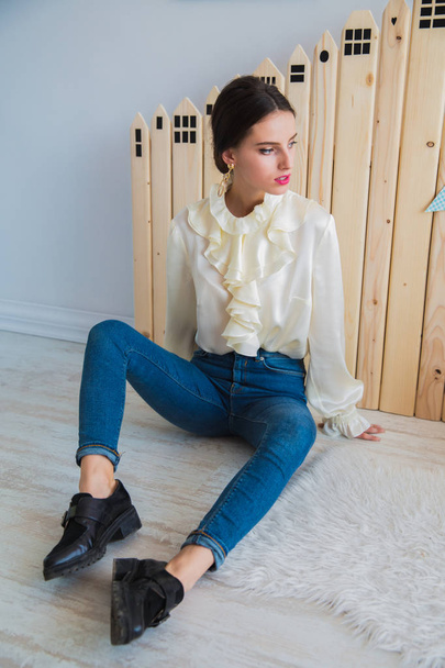 The gorgeous, serious, stylish young woman sitting on the floor indoor and looking aside - Photo, image