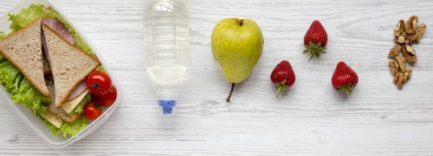 Taze organik sebze sandviç, ceviz, şişe su ve beyaz tahta masada, yukarıdaki meyve sağlıklı okul beslenme çantası. Düz yatıyordu, genel gider, en iyi görünümü. - Fotoğraf, Görsel