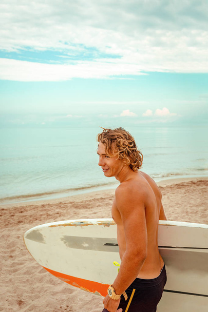 Beau homme marcher avec planche de surf blanc blanc attendre la vague pour surfer spot au bord de l'océan. Concept de sport, fitness, liberté, bonheur, nouvelle vie moderne, hipster
. - Photo, image