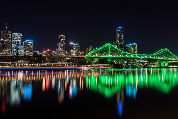 Weergave van felle gloeiende lichten van brug en wolkenkrabbers weerspiegelen in rivier in nachttijd - Foto, afbeelding