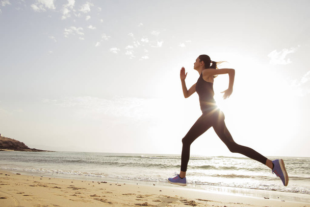Молода спортивна жінка біжить вранці на пляжі
. - Фото, зображення