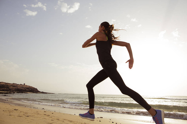 Молода спортивна жінка біжить вранці на пляжі
. - Фото, зображення