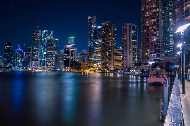 Gloeiende moderne hoogbouw gebouwen in nachttijd op de oever van de rivier van de stad weerspiegelen in water, Brisbane - Foto, afbeelding