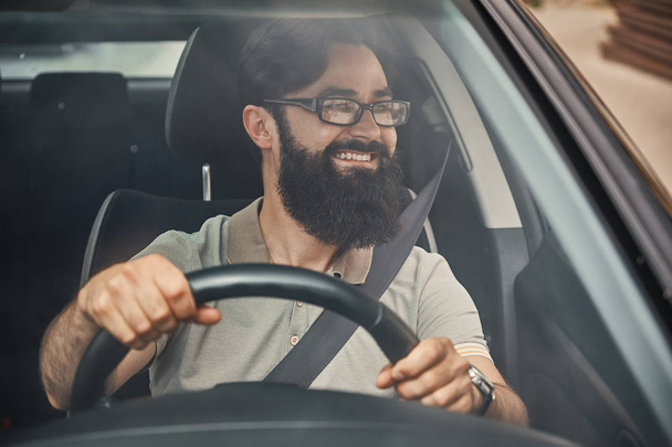 Mladý atraktivní muž řízení vozidla, při pohledu na krajinu, vidět skrze čelní sklo. Happy řidič, hospodářství ruce na volant s širokým krásný úsměv. - Fotografie, Obrázek