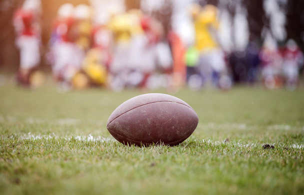 Close up of an american football on the field, players in the background - Foto, immagini