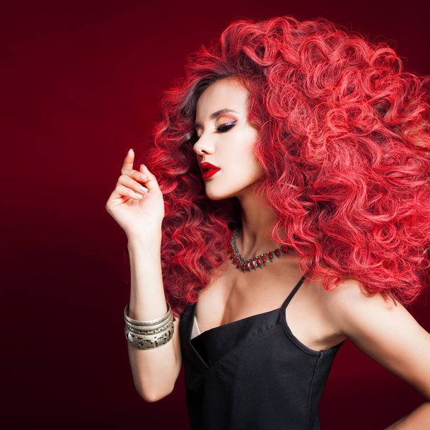 Portrait of a young attractive woman with a very lush hairstyle. Red hair on a red background. - Photo, image