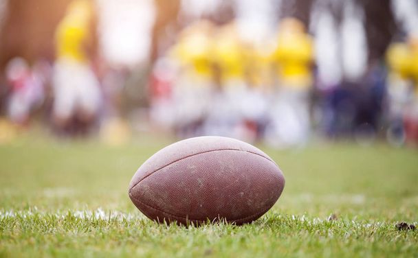 Close up of an american football on the field, players in the background - Foto, imagen