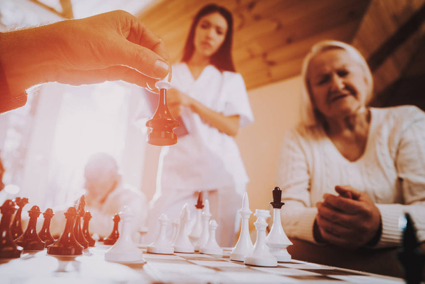 Play Chess. Nurse. Stand Nearby. Sitting Woman. Senior Man and Woman. Nursing Home. Black. Doctor. Asian. Rehabilitation. Elderly. Male. Patient. Patient on a Wheelchair. Young and Old People. - Photo, image