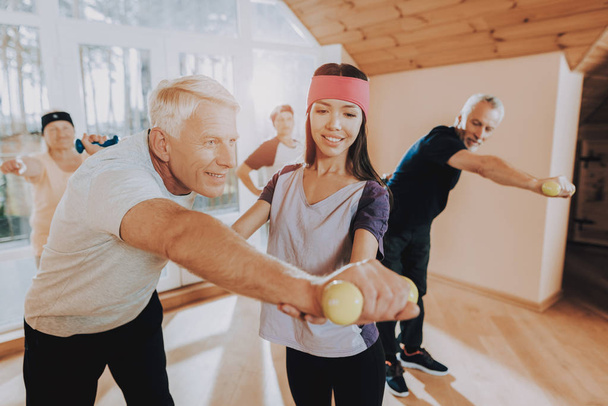 Young Instructor. Men. Active Retiree. Have Fun. Wearing Sport Uniform. Healthcare Lifestyle. Exercises. Group Elderly Women. Therapeutic Gymnastics. Engaged with them. Nursing Home. Smiling Patient. - Photo, Image