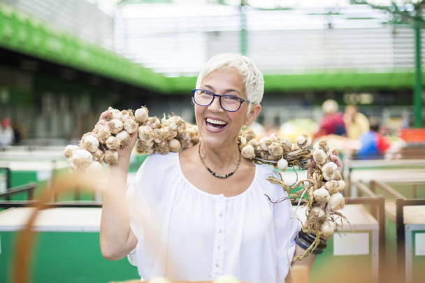 Retrato de mujer mayor comprando mucho ajo en el mercado
 - Foto, imagen