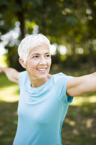 Mujer mayor haciendo ejercicio tretching brazo en el parque en el día de verano
 - Foto, Imagen