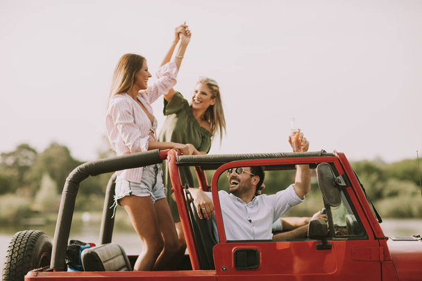 Happy friends having fun in convertible car at vacation by river - Foto, imagen
