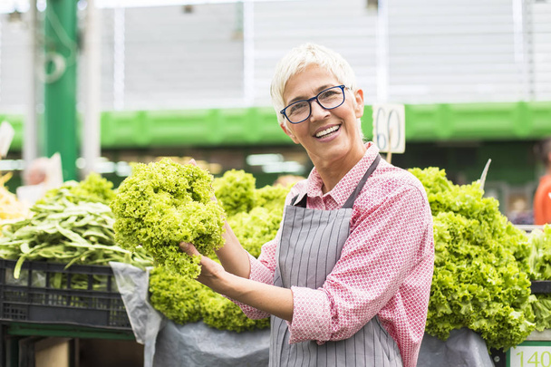 Portrait of senior woman sells lettuce on marketplace - Photo, Image