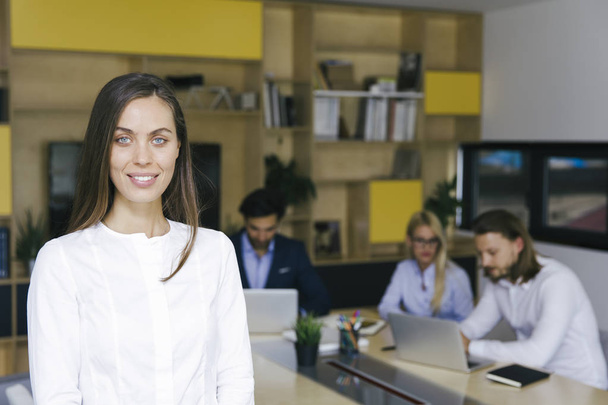 Portrait of young businesswoman standing in the office and other young business people working in the background - Photo, Image