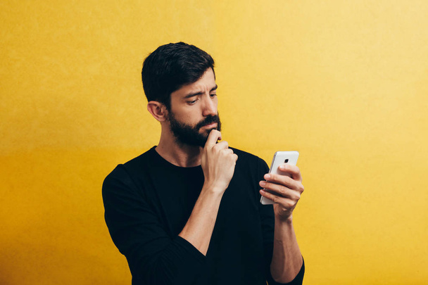 Shocked bearded man using mobile phone over yellow background - 写真・画像