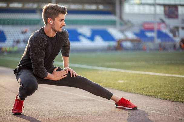 man stretches the body before running on race track in stadium - 写真・画像