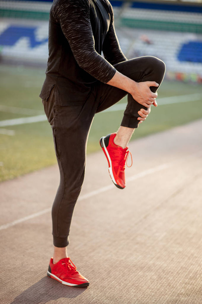man stretches the body before running on race track in stadium - Valokuva, kuva