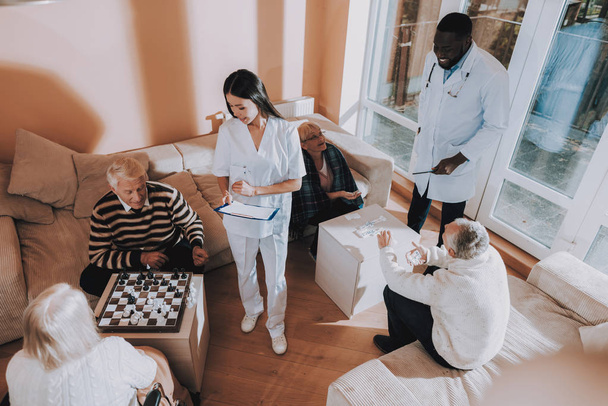 Play Chess. Black. Doctor. Asian. Nurse. Patient. Senior Man and Woman. Nursing Home. Stand Nearby. Rehabilitation. Elderly. Male. Patient on a Wheelchair. Sitting Woman. Young and Old People. - Fotoğraf, Görsel