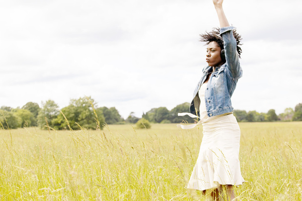 νεαρή μαύρη γυναίκα, χορό σε ένα ψηλό γρασίδι πεδίο, ενώ ακούτε μουσική - Φωτογραφία, εικόνα