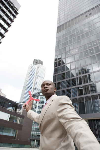 Businessman throwing a boomerang while standing in the middle of the financial district. - Photo, Image