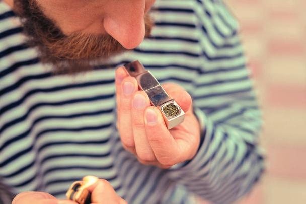 Bearded man holding lighter and tiny metal pipe before smoking - Fotó, kép