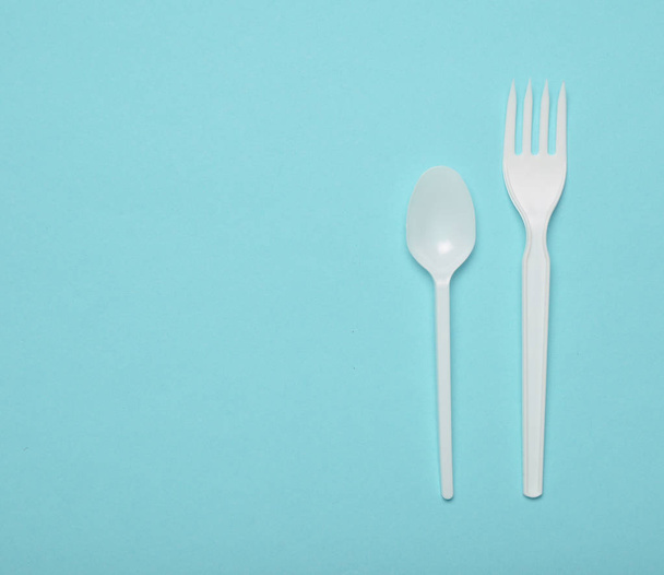 White plastic cutlery for picnics on a blue background. Disposable spoon, fork. Top view, copy space - Photo, image