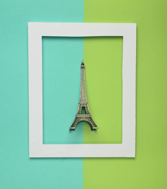 Estatueta de lembrança da torre Eiffel em uma moldura branca em um fundo pastel colorido. Tendência minimalista. Vista superior
 - Foto, Imagem