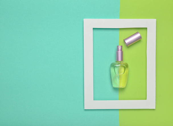 Pastel renkli bir arka plan üzerinde beyaz bir çerçeve içinde bir parfüm şişesi. Minimalist eğilim. Üstten görünüm - Fotoğraf, Görsel