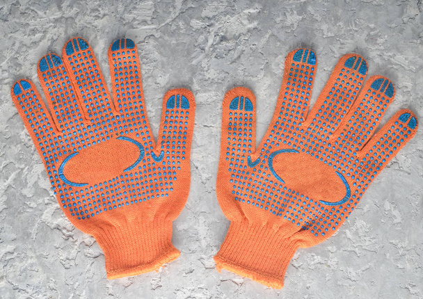 Оранжевые рабочие перчатки на сером бетонном фоне. Вид сверху
 - Фото, изображение