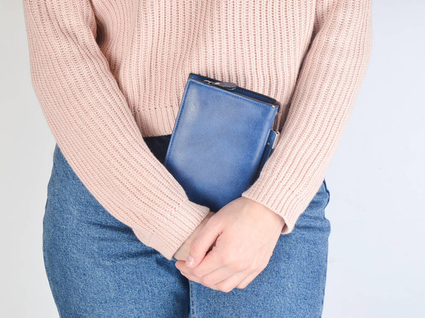 Young fit girl in jeans and a sweater is holding her wallet on a white background. - Photo, Image