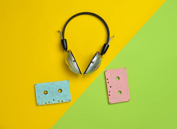 Vezeték nélküli fejhallgató és a színes pasztell papír alapon audio kazetták. Minimális creative art. Zenei retro rezgéseket. Szemközti nézet - Fotó, kép