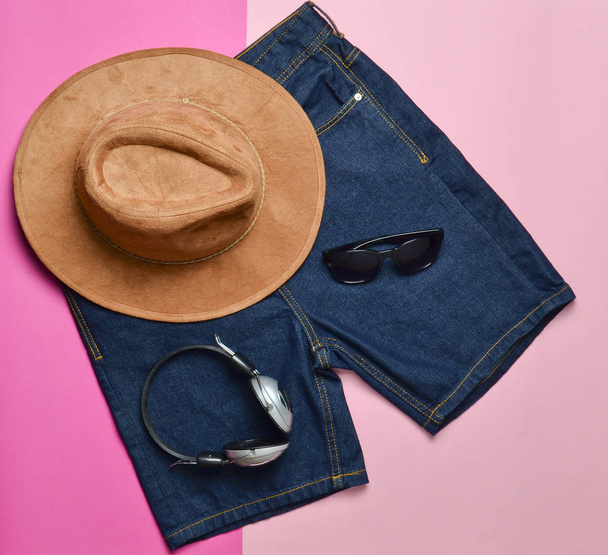 Trendy accessories and clothes on a pile of paper background. Felt hat, glasses, headphones, shorts, top view, fashionable look - Valokuva, kuva