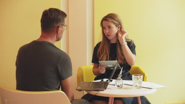 Бізнес-леді і чоловік на перерві зі своїм планшетом сидять в кафе з жовтими стінами і обговорюють проект
 - Кадри, відео