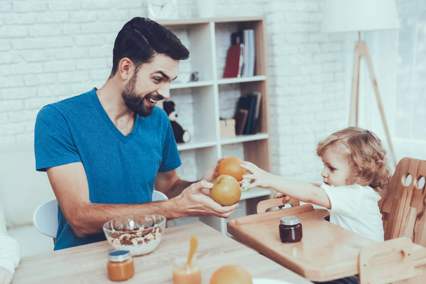 Citrus Fruits. Child on Chair. Spends Time. Happy Together. Sweet Baby. Having Breakfast. Enjoy. Jam. Childhood. Boy. Baby with Bright Hair. Smile. Leisure Time. Smiling Kids. Father. Man. Home Time. - Photo, image