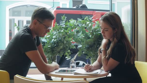 Una mujer de negocios y un hombre en su descanso con su tableta se sientan en un café con paredes amarillas y discuten un proyecto
 - Metraje, vídeo