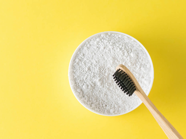 A jar of tooth powder and a wooden brush with black bristles on a yellow background. Oral care products. The view from the top. Flat lay. - Photo, Image