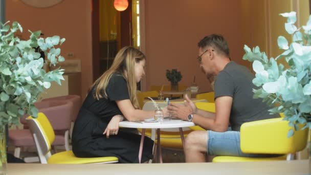 Бізнес-леді і чоловік на перерві зі своїм планшетом сидять в кафе з жовтими стінами і обговорюють проект
 - Кадри, відео
