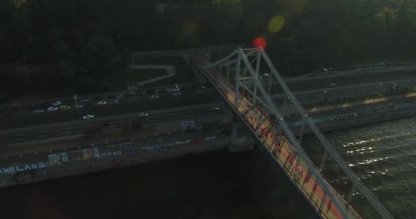fliegt bei Sonnenuntergang über eine Fußgängerbrücke über den Fluss. Drohnenschuss: Kiew, Ukraine - Filmmaterial, Video
