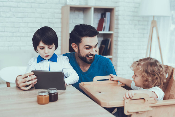 Tablet. Spends Time. Happy Together. Leisure Time. Smiling Kids. Father. Flakes with Milk. Delisious Food. Father Two Boys. Breakfast. Man. Child on Chair. Jam. Smile. Home Time. Citrus Fruits. - Foto, Imagem