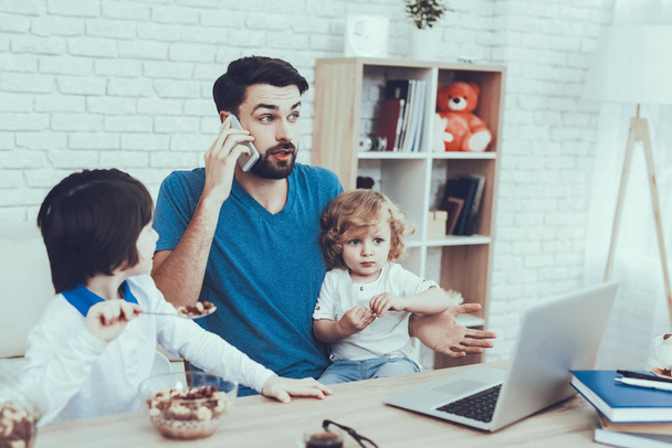 Happy Together. Works at Home. Having Breakfast. Upbringing. Looks After Children. Spends Time. Leisure Time. Smiling Kids. Father. Father Two Boys. Man. Home Time. Baby with Bright Hair. Laptop. - 写真・画像