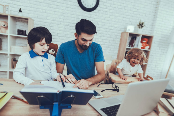 Works at Home. Laptop. Father Two Boys. Homework. Upbringing. Looks After Children. Spends Time. Happy Together. Leisure Time. Smiling Kids. Father. Man. Home Time. Baby with Bright Hair. - 写真・画像