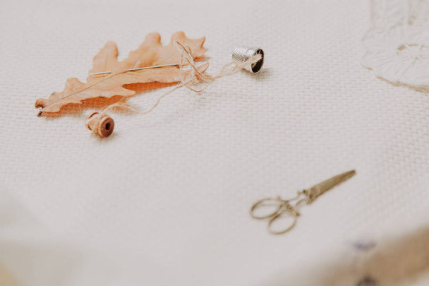 Herbststilleben. ein großes gelbes Eichenblatt und eine Spirale mit einem Faden lagen auf einem weißen Leinen. In der Nähe liegt Fingerhut und Schere - Foto, Bild