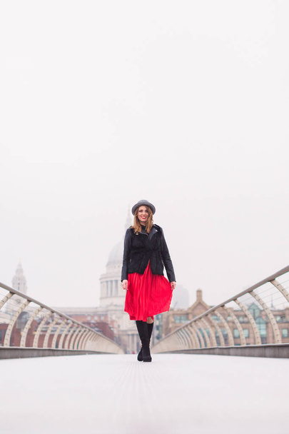 The young elegant cheerful woman in hat walking on the bridge outdoors - 写真・画像