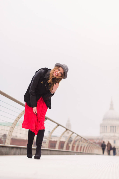 The young elegant joyful lady in hat standing on the bridge outdoors - Fotografie, Obrázek