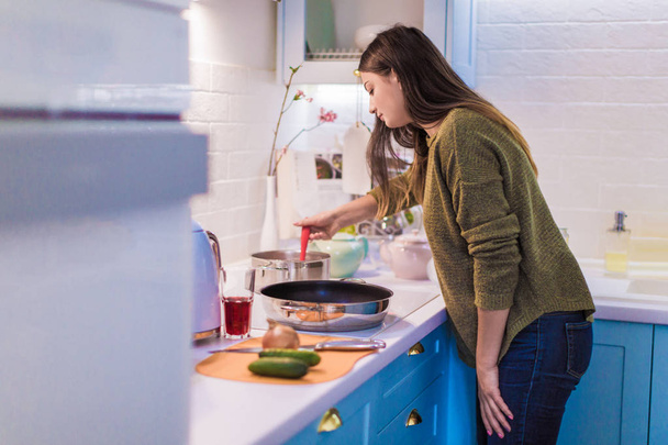 Вид збоку на молоду щасливу жінку, яка стоїть на кухні і готує
 - Фото, зображення