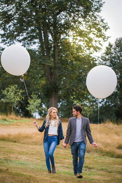 The young happy couple walking outdoor and holding the white balloons in hands - Fotó, kép